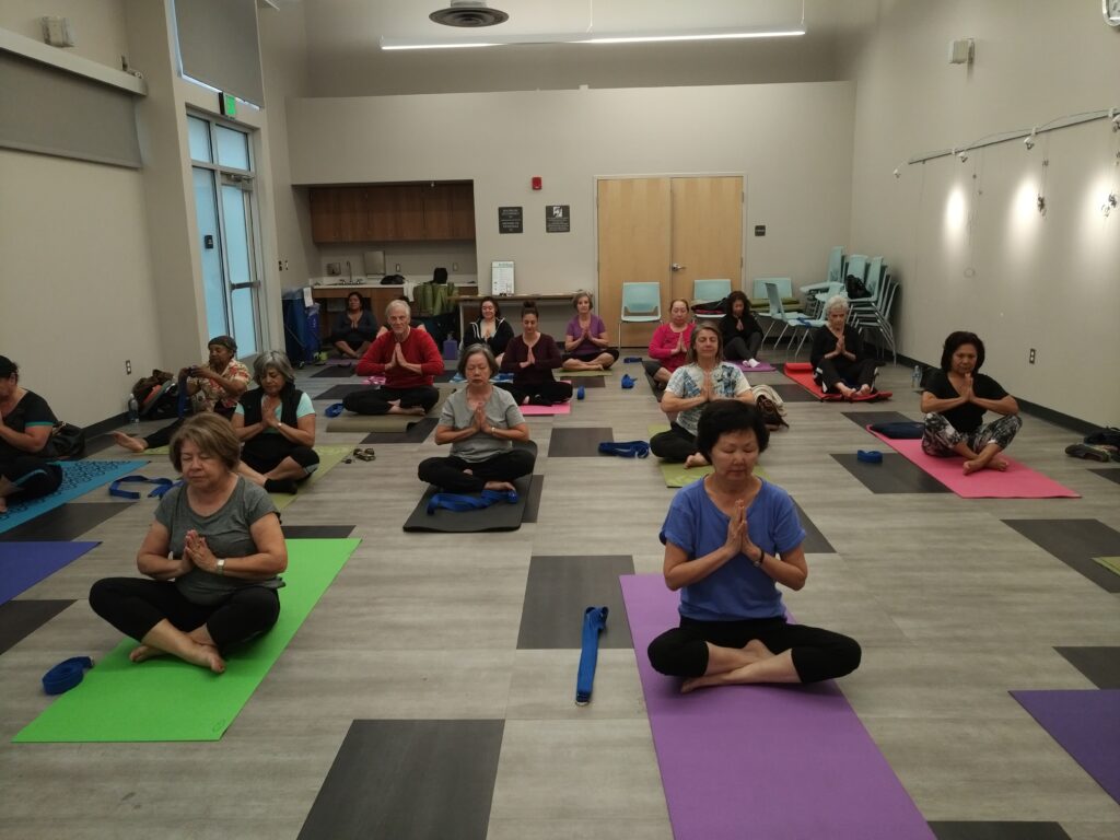 Over a dozen people are seated on yoga mats in the Betty Rodriguez meeting room, all of them with their eyes closed, legs crossed, and hands in prayer position.